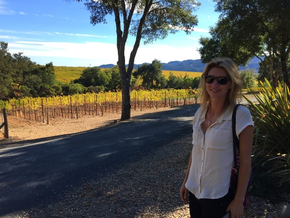 a woman standing on a road with vineyard in the background