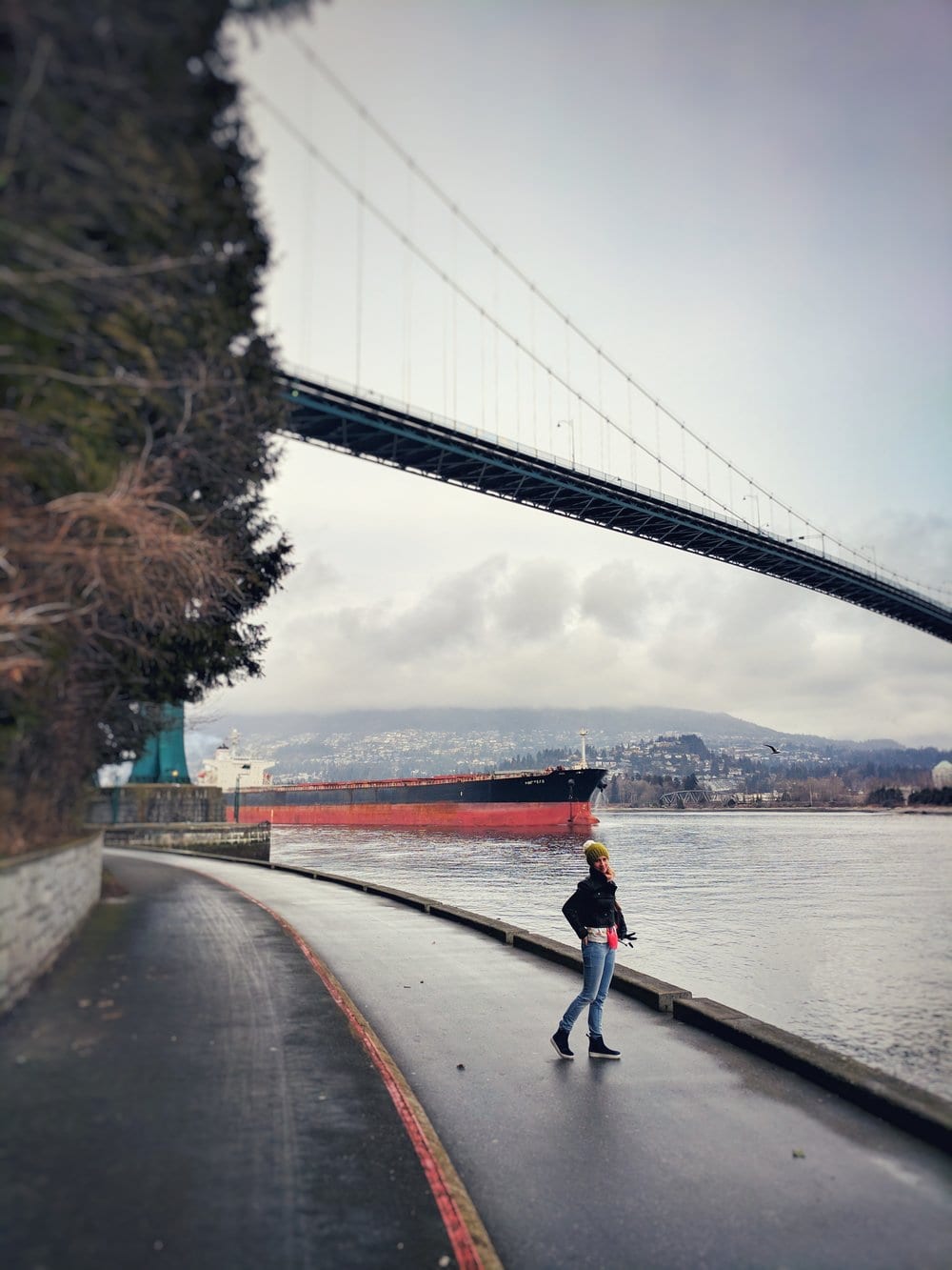 a woman walking on a sidewalk near a bridge