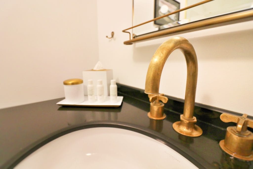 a sink with gold faucet and a tray of toiletries