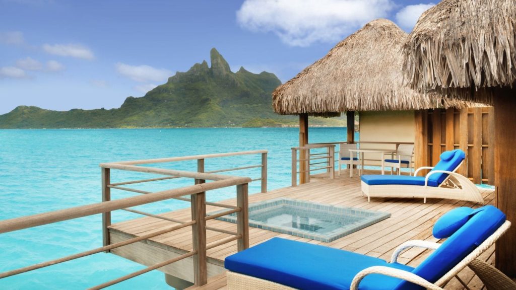 a deck with chairs and a hut on the water with Bora Bora in the background
