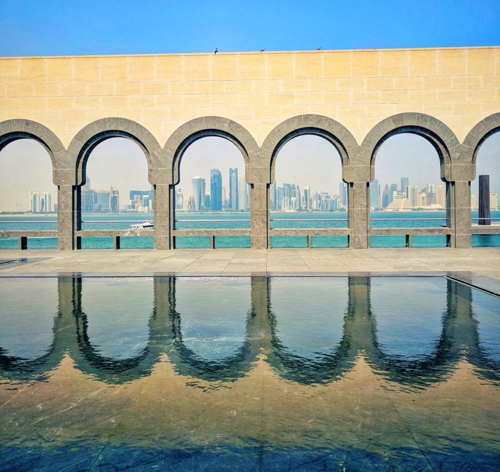 a pool with arches and a city in the background