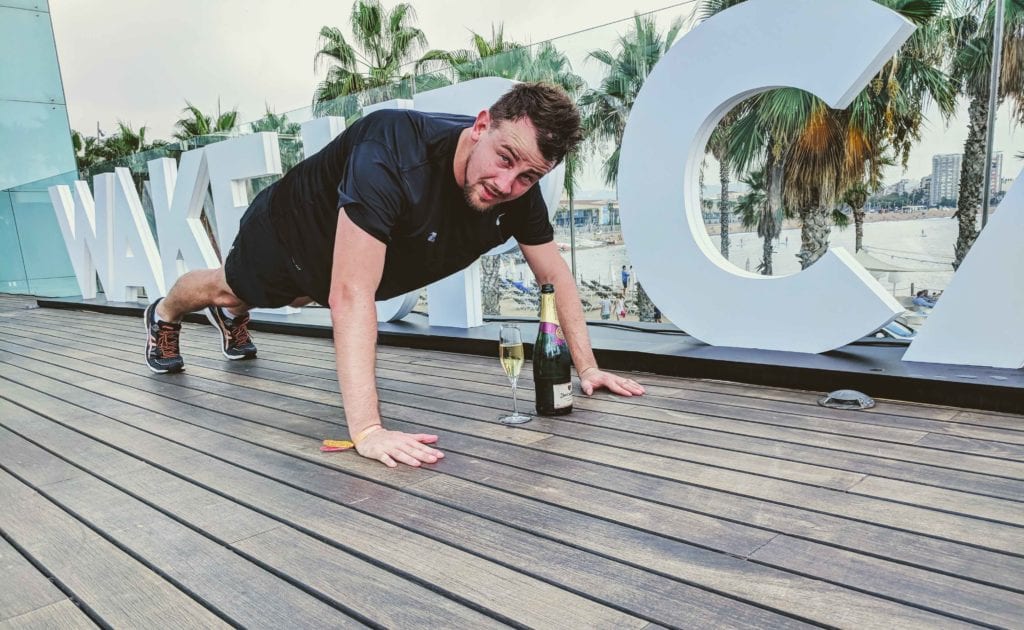 a man doing push ups on a deck with a glass of champagne