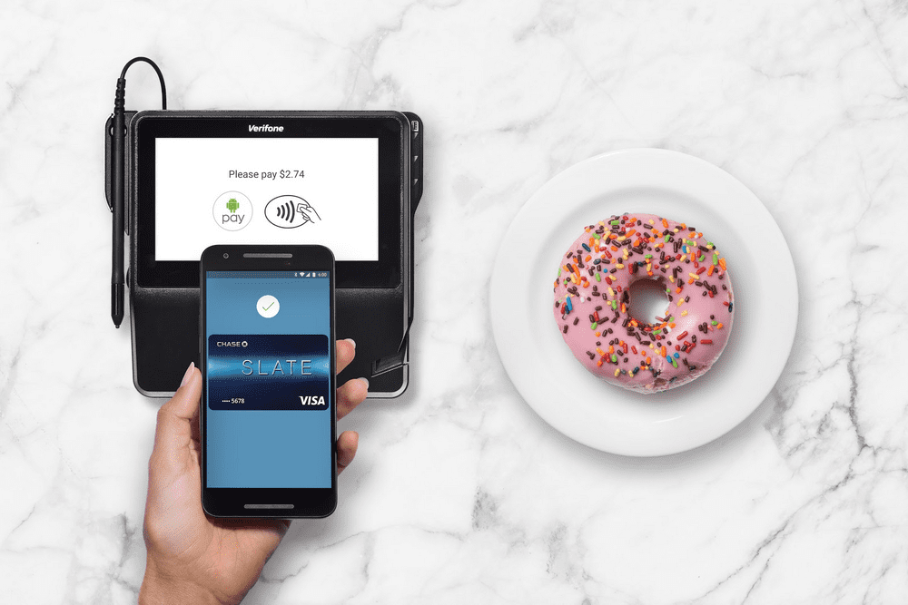 a hand holding a phone next to a donut