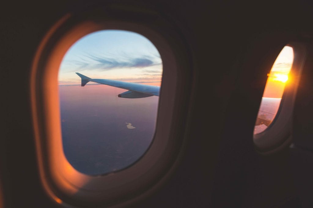 Sunset aerial view through airplane window over wings. Flying at sunset and looking out of the window and enjoying the panoramic view. Travel and transportation concepts