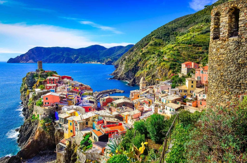a colorful buildings on a hillside by a body of water with Cinque Terre in the background