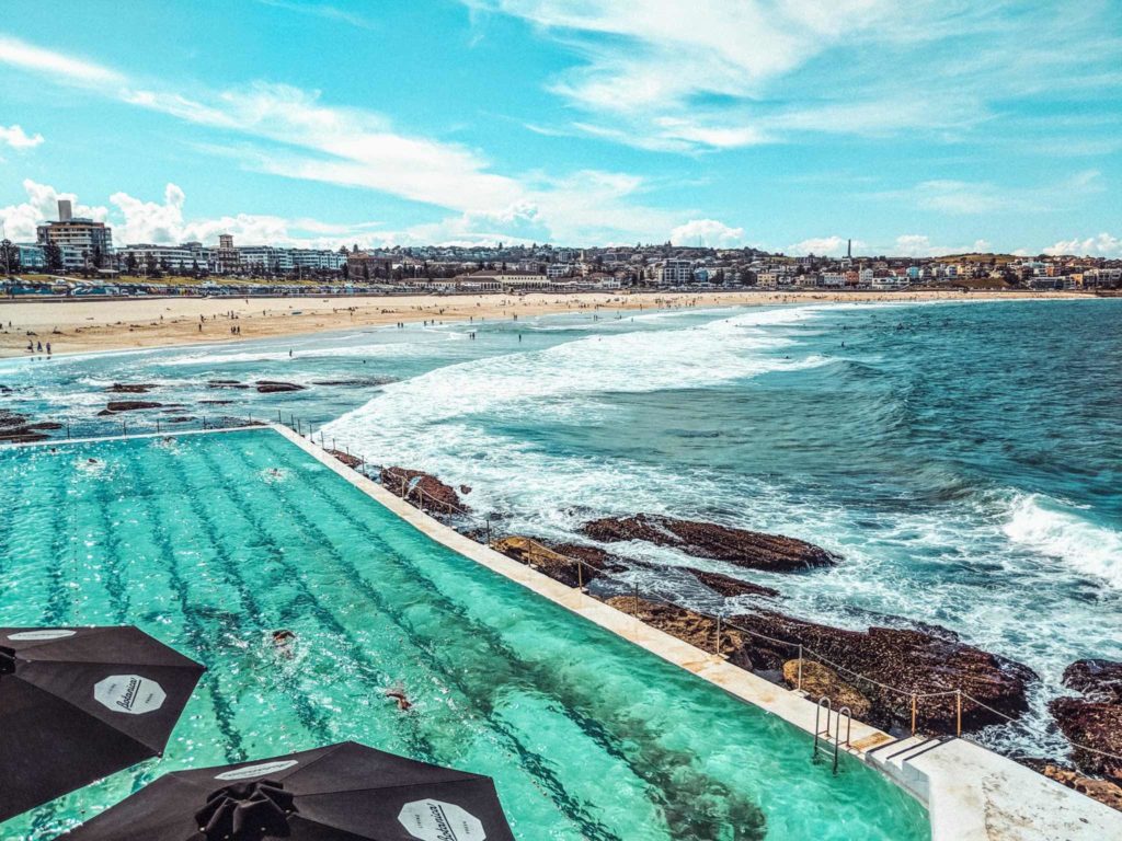 a pool with umbrellas and a beach in the background with Bondi Beach in the background
