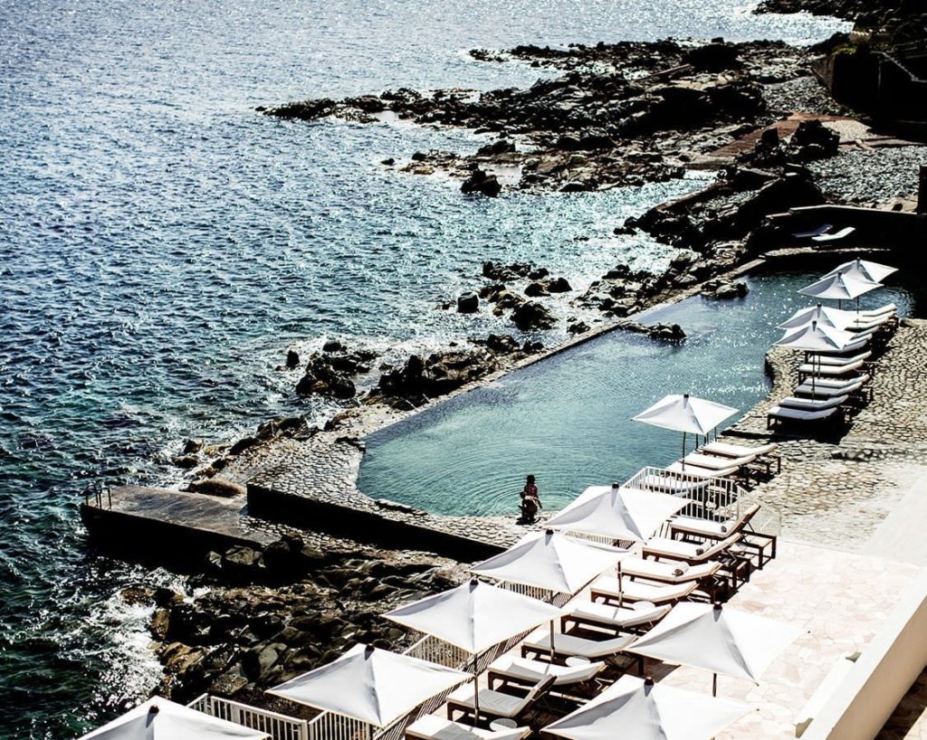 a pool with white umbrellas and chairs on the side of a rocky beach