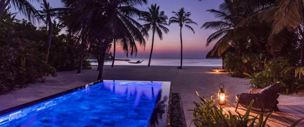 a pool on a beach with palm trees and a sunset