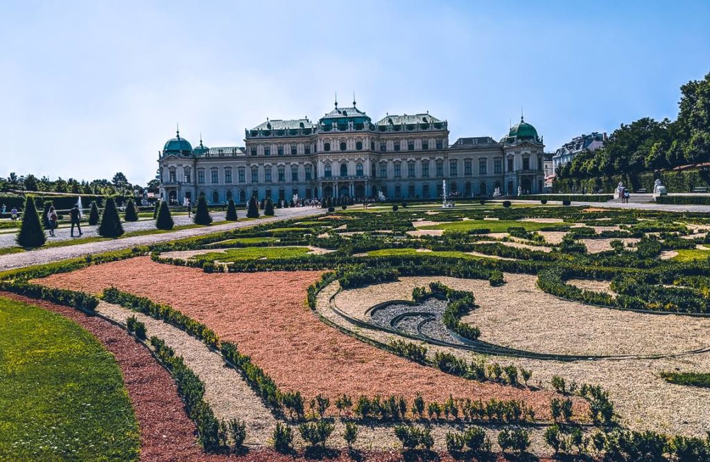a large white building with a garden in front of it with Belvedere, Vienna in the background