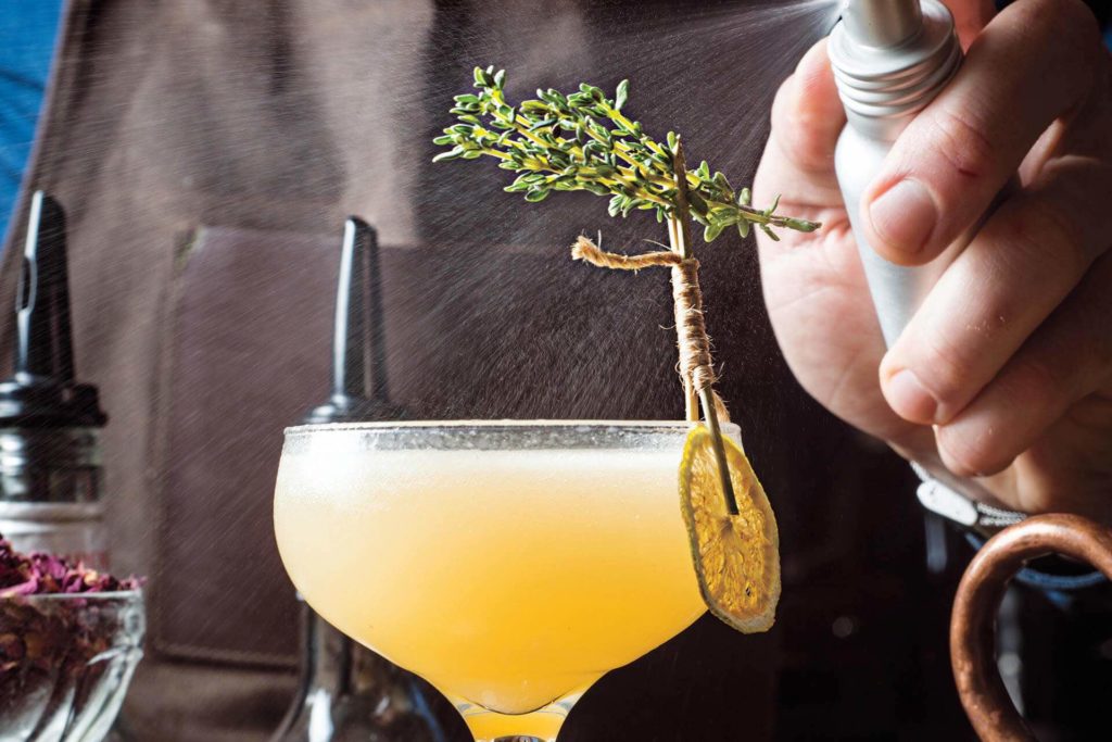 a person spraying a drink with a sprig of thyme