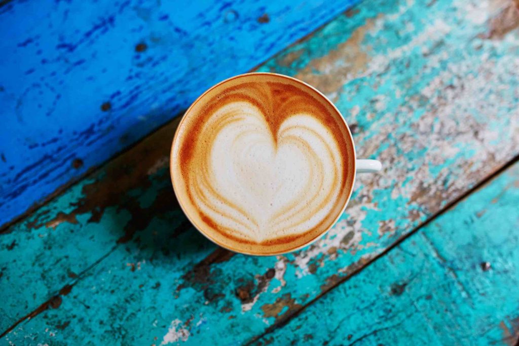 Cup of fresh coffee with heart form milk drawing on blue wooden table, view from above, flat lay
