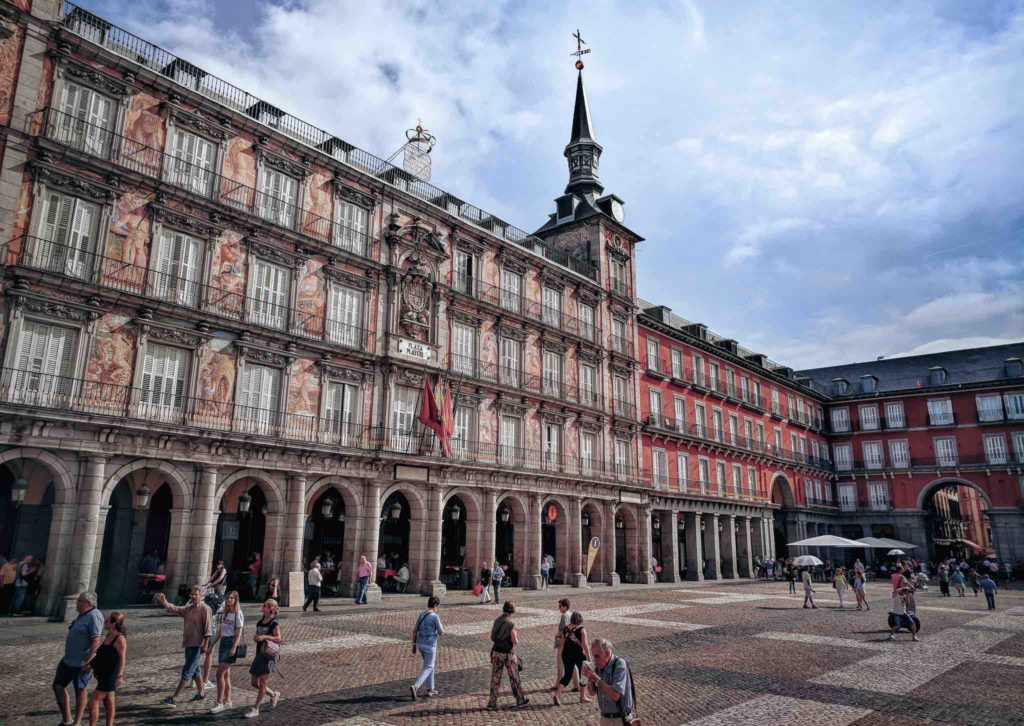 a group of people walking in a courtyard with Plaza Mayor, Madrid in the background