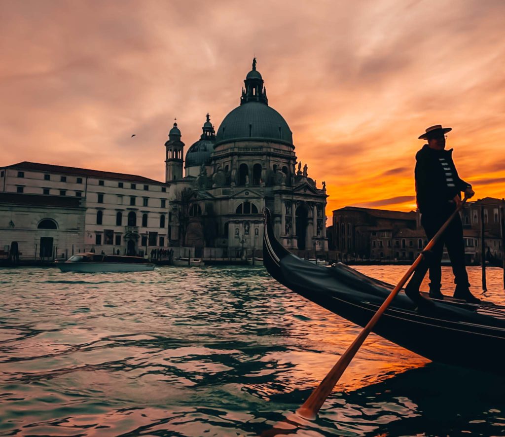 a man in a gondola on the water with a building in the background