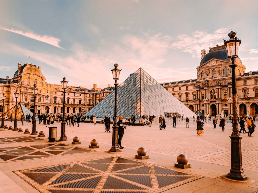 a large glass pyramid in a courtyard with Louvre in the background