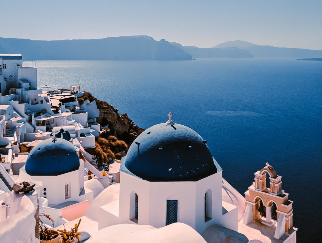 a white buildings with blue domes and a body of water with Santorini in the background