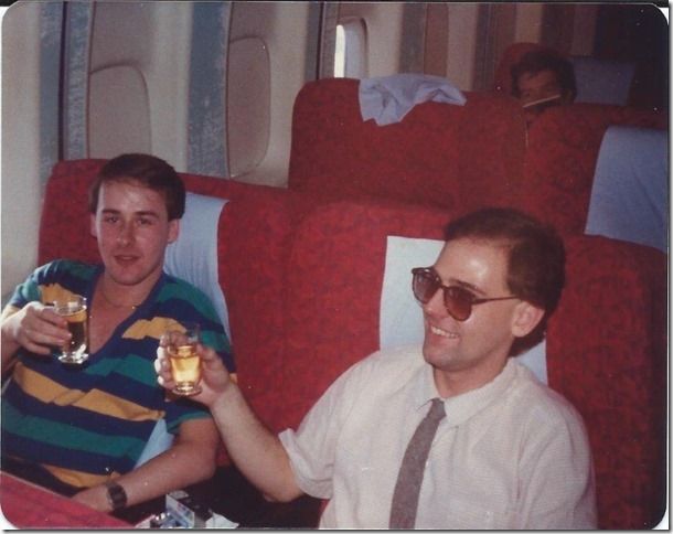 two men sitting in a plane holding drinks