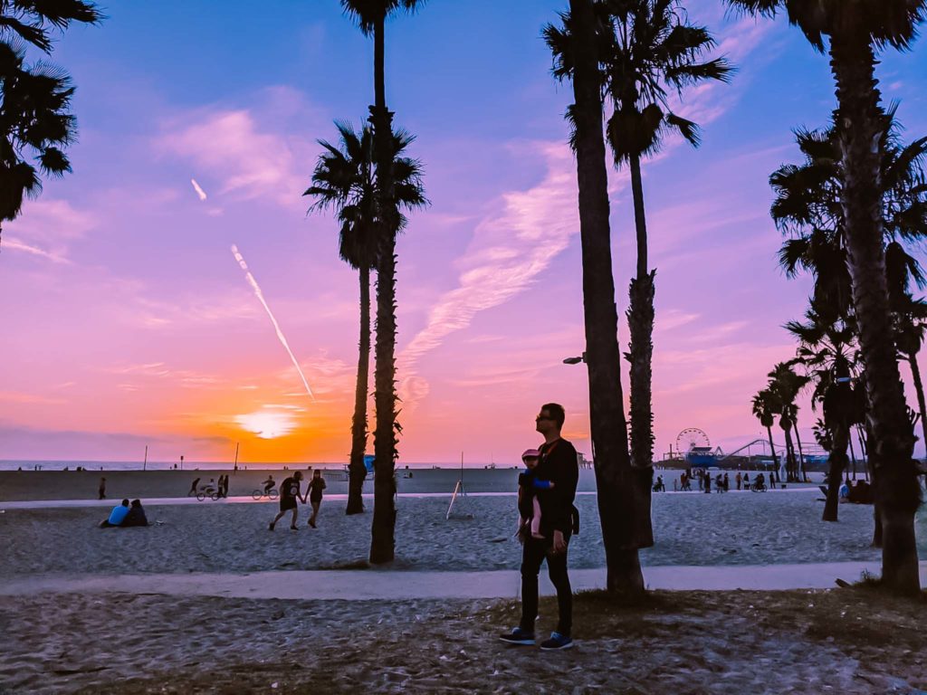 a man standing on a beach with palm trees and a sunset