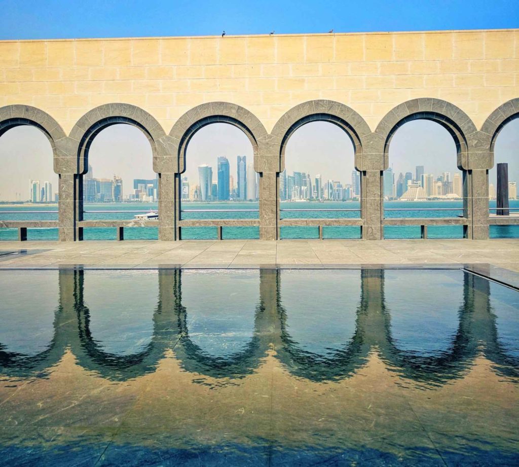 a pool with arches and a city in the background