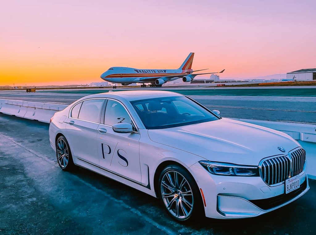 a white car on a runway with an airplane in the background