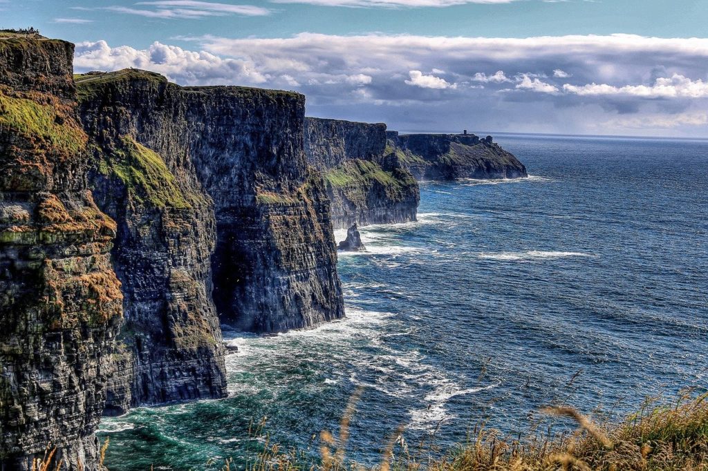 a cliff with grass and water with Cliffs of Moher in the background