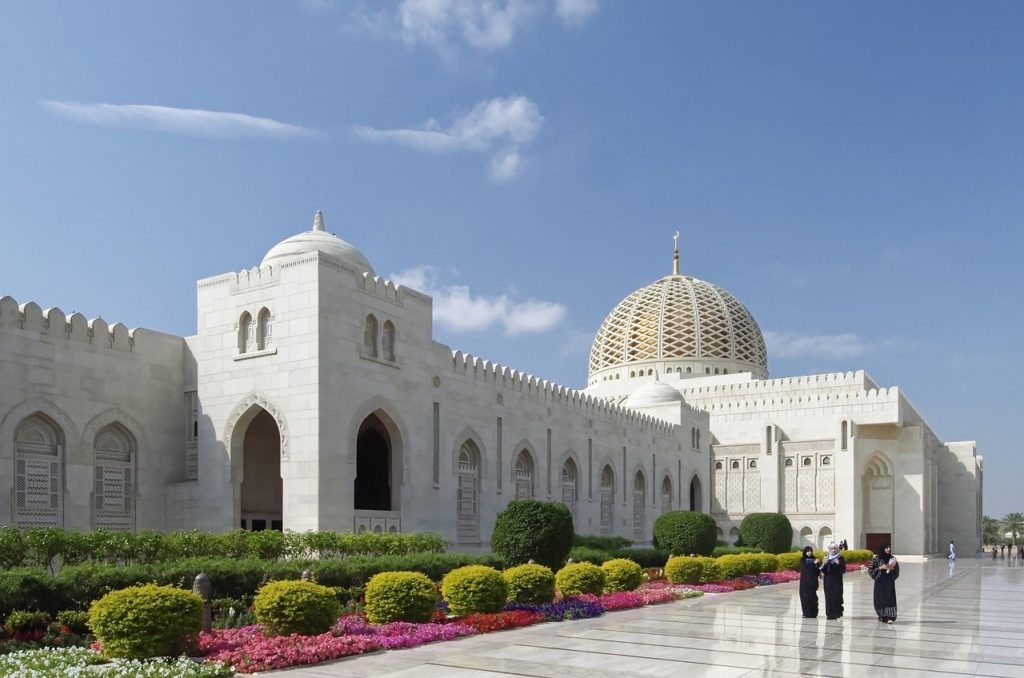 a white building with a dome and a tiled roof with Sultan Qaboos Grand Mosque in the background