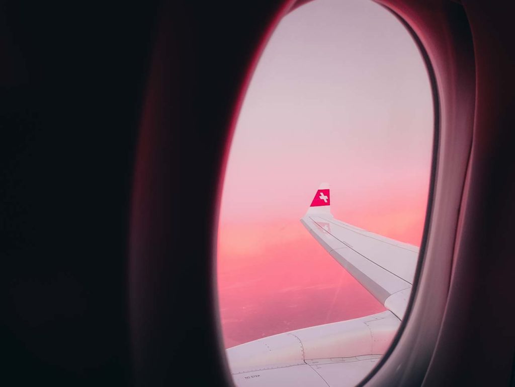 an airplane wing with a red and white tail and a pink sky
