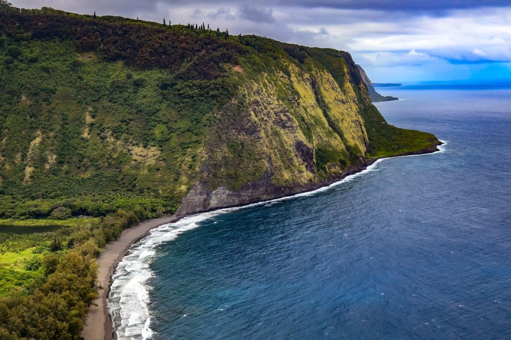 a large body of water with a cliff and trees with Waipio Valley in the background