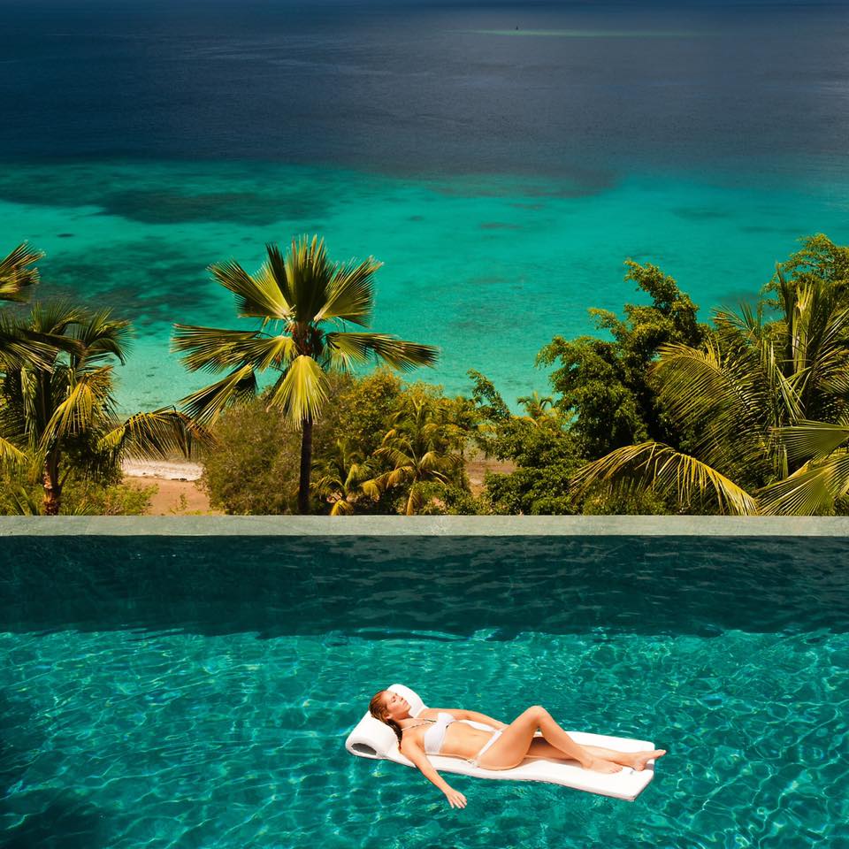 a woman lying on a floating bed in a pool with palm trees