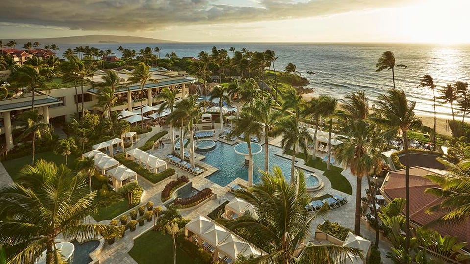 a resort with a pool and palm trees by the ocean