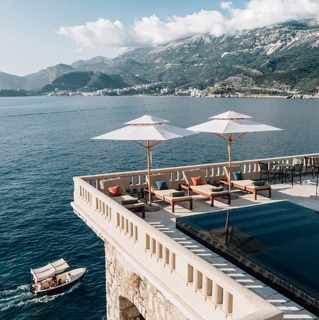 a pool with umbrellas and chairs on a ledge overlooking a body of water