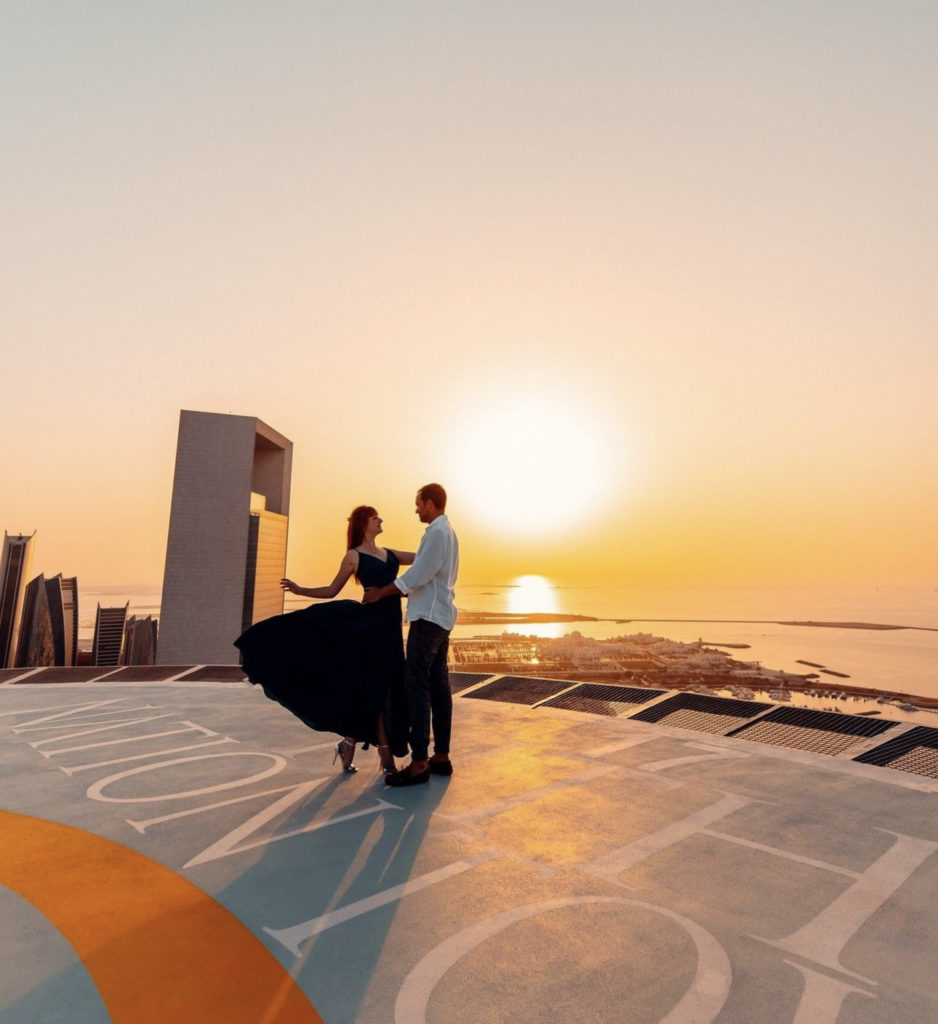 a man and woman standing on a rooftop with a sunset in the background