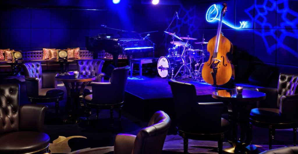 a room with a stage and chairs and a piano and a double bass